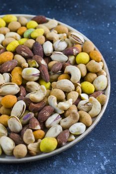 Nuts mix, beer snack on the bowl. Studio shoot. Cashews and coasted nuts on the blue background. Colorful nuts set.