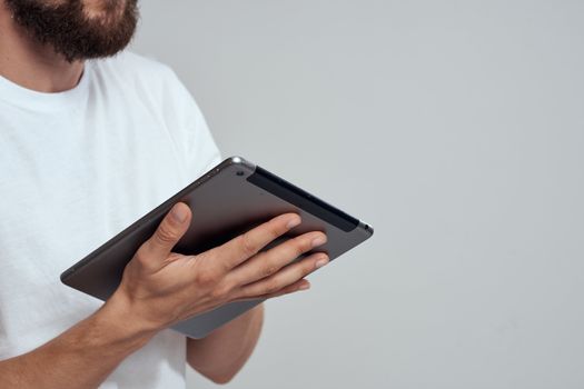 Tablet with a touch screen on a light background male hands white t-shirt cropped view. High quality photo