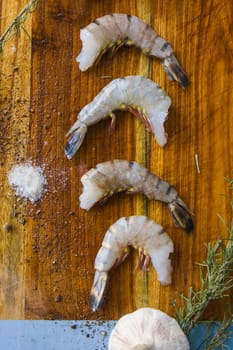 Raw shrimps on the wooden board with salt, dry pepper and rosemary, natural light.