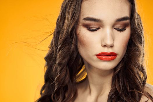 Beautiful brunette naked shoulders bright makeup red lips hairstyle close-up yellow background. High quality photo