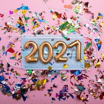 Gold numbers 2021 on face mask, pink background and confetti. Happy new pandemic year