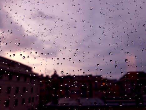 Genova, Italy - 10/22/2020: Water​ rain​ drops​ on​ glass​ background.​ Rain​ drops​ on​ a​ Windows. Hdden sunset in autumn after rain.