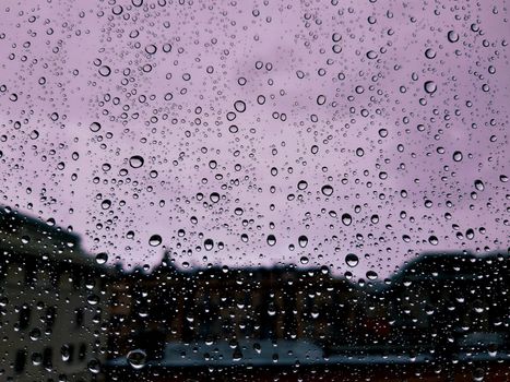 Genova, Italy - 10/22/2020: Water​ rain​ drops​ on​ glass​ background.​ Rain​ drops​ on​ a​ Windows. Hdden sunset in autumn after rain.