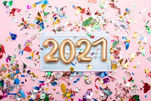 Gold numbers 2021 on face mask, pink background and confetti. Happy new pandemic year
