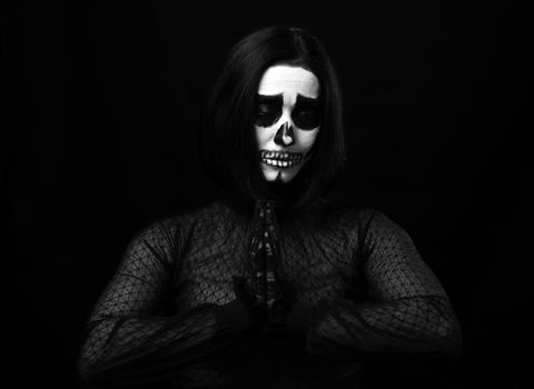 woman with skeleton make-up stands in prayer pose, black background 