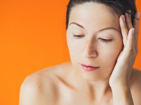 Portrait of woman with freckles on orange monochrome background. No make up. Natural beauty on bright and colorful backdrop. Banner with copy space.