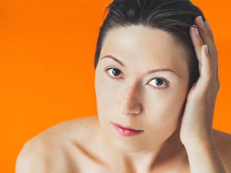 Portrait of woman with freckles on orange monochrome background. No make up. Natural beauty on bright and colorful backdrop. Banner with copy space.