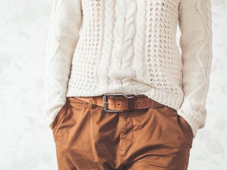 Woman in cable-knit white sweater with Scandinavian pattern and brown chinos trousers with leather belt. Casual clothes for snuggle weather. Modern urban fashion.