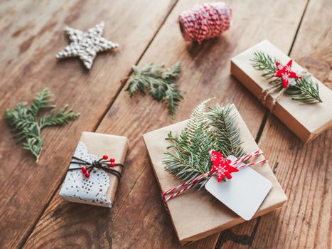 Christmas DIY presents wrapped in craft paper with fir tree twigs. Red decorations in shape of Christmas tree, stars. New Year gifts on wooden background. Winter holiday spirit.