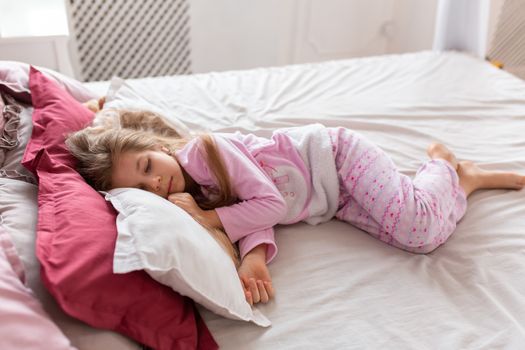 A little girl in pink pajamas is fast asleep on a comfortable bed.