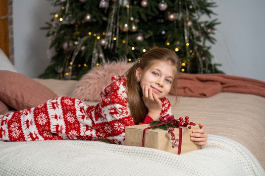 A little girl in pajamas early in the morning found a present from Santa under the tree. Christmas magic fairy tale. Happy childhood.