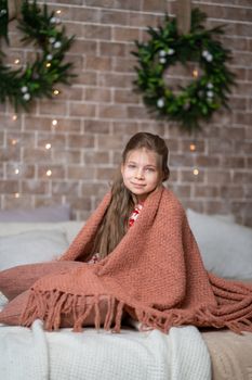 A little girl keeps warm under a cozy knitted blanket.