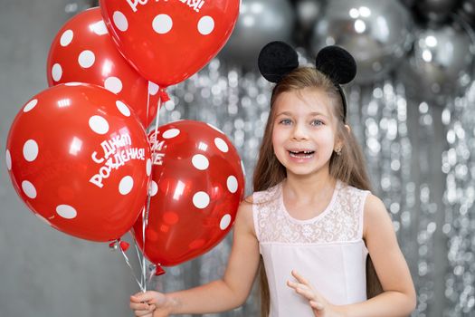 Little girl with red balloons celebrates her birthday.