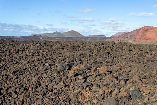 Volcanic landscape with lava field in the foreground and mountain range with different red and brown colours in the background on canary island Lanzarote, Spain