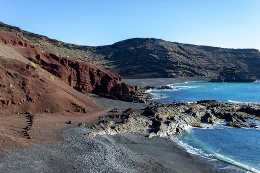 Panoramic view on the coastline of El Golfo with red and black colored volcanic rock formations and lava fields in the southwest of canary island Lanzarote