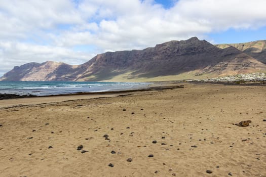 Coastline and sand beach Playa de Famara with mountain range and ocean waves on canary island Lanzarote, Spain