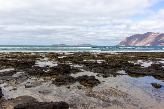 Coastline and sand beach Playa de Famara with mountain range and ocean waves in the north west of canary island Lanzarote, Spain