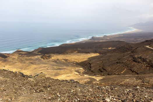Panoramic view at the coastline in the natural park of Jandia (Parque Natural De Jandina) on canary island Fuerteventura, Spain with gravel, lava rocks and rough sea with waves and mountain range in the background