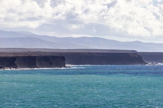 Panoramic view at the coastline of El Cotillo on canary island Fuerteventura, Spain with  lava rocks and mountain range in the  background