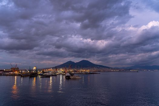Naples harbor at sunset with shipyards and Vesuvius volcano in Italy.