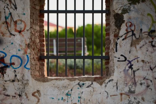 Window with rusty bars and painted graffiti of an abandoned building in a park or forest