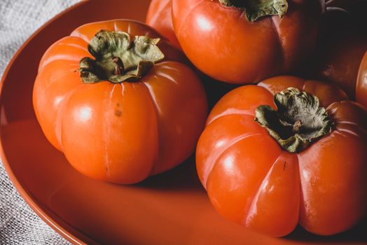 Few fresh persimmons on orange plate over white textile