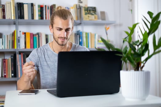 Attractive young man sitting at the table at home working with a laptop with happy face and smiling with a smile