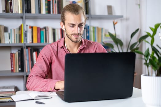 Attractive young man sitting at the table at home working with a laptop with happy face and smiling with a smile