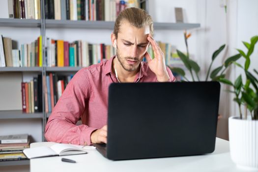 Attractive young man sitting at the table at home working with a laptop and looking worried