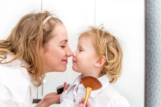 Portrait of woman doing makeup to her daughter in the bedroom on the bed.