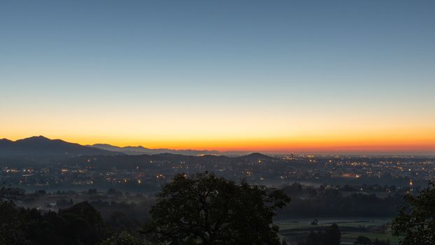 A clear sky lights up during the sunrise over the plain with the last city lights, Italian landscape