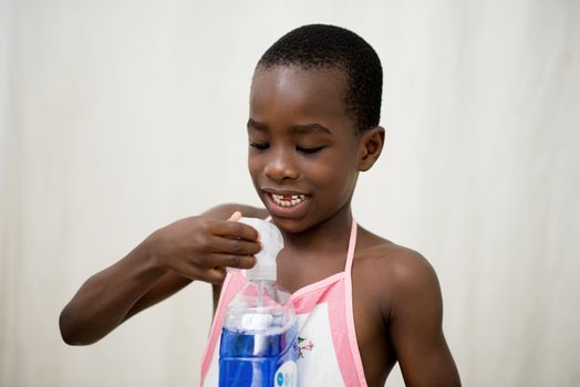 smiling little boy standing in studio and wearing apron plays with bottle of liquid soap