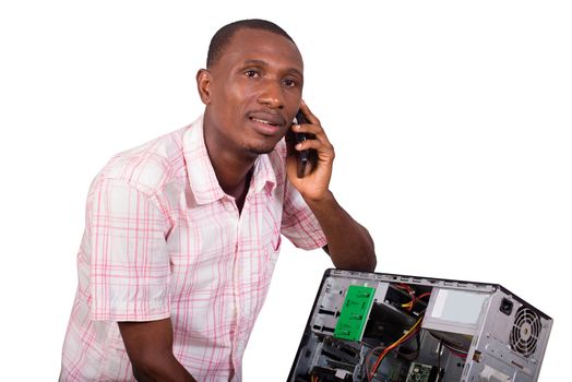 Young technician leaning against a broken computer and speaking on the phone