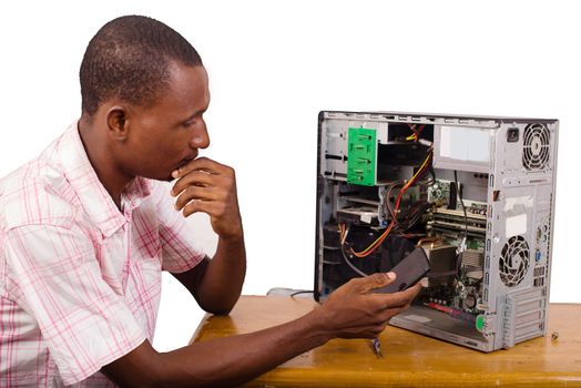 young technician sitting thinking with a desktop computer in front of him and holding a mobile phone.