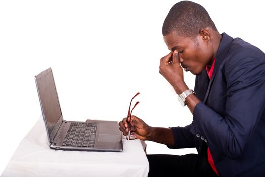 Tired african american employee in formal attire holding glasses rubbing his eyes and massaging the bridge of the nose to release tension after long hours of work in the office