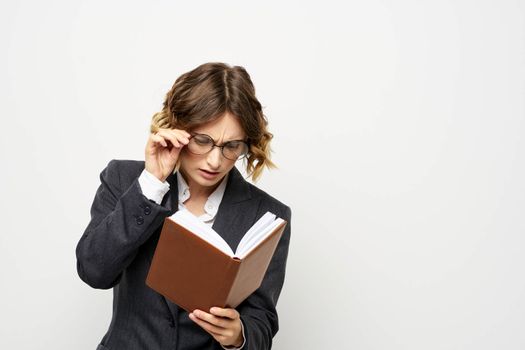 Woman at work with book in hand light background classic suit glasses head. High quality photo