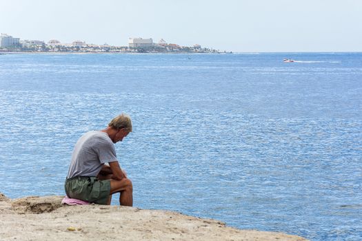 Spain, Tenerife-September 11, 2016: an Elderly man sitting on the rocks by the sea and looking down from the cliff