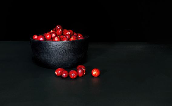 A bunch of cranberrries in a black, cast iron bowl, with black background. Shot in low key style.