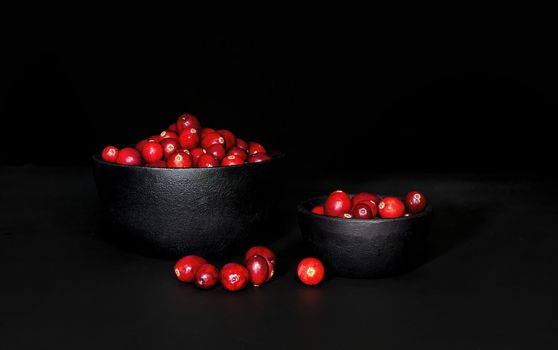 A bunch of cranberrries in 2 black, cast iron bowls, with black background. Shot in low key style.