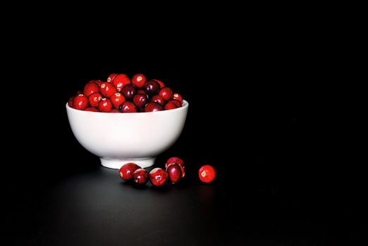 A bunch of cranberrries in a white porcelain bowl, with black background. Shot in low key style.