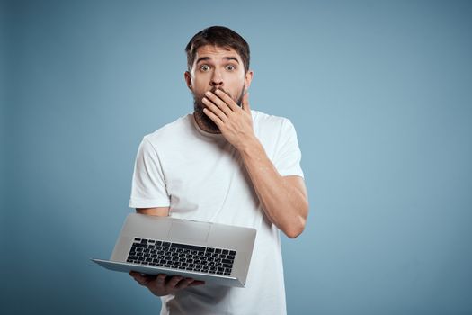 Emotional man with laptop in hands on blue background monitor keyboard internet model cropped view. High quality photo