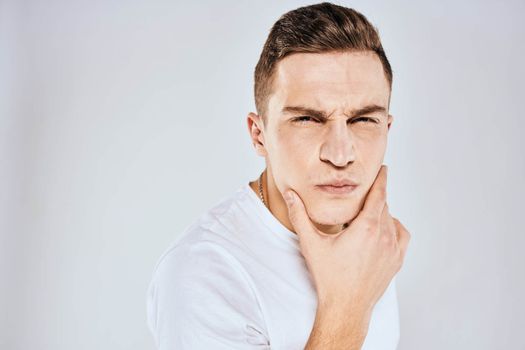 Emotional man in a white t-shirt holds his hand on his face light background. High quality photo