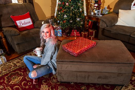 A gorgeous blonde model enjoys the holiday season at home with a Christmas tree and presents