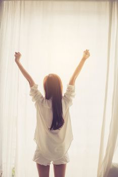 Beautiful young asian woman stretch and relax in bed after wake up morning at bedroom, back view, new day and resting for wellness, lifestyle concept.