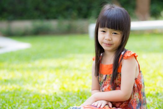 Beautiful portrait little girl asian of a smiling sitting on green grass at the park, kid leisure and joyful in outdoor.