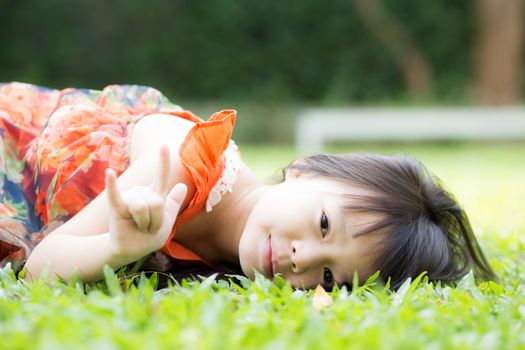 Beautiful portrait little girl asian of a smiling lying on green grass at the park, kid  leisure and joyful in outdoor.