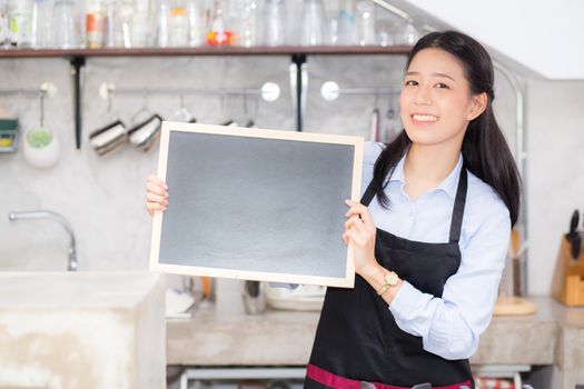 Portrait of beautiful young barista, asian woman is a employee standing holding chalkboard in counter coffee shop, service concept.