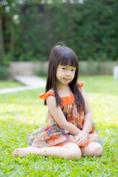 Beautiful portrait little girl asian of a smiling sitting on green grass at the park, kid leisure and joyful in outdoor.