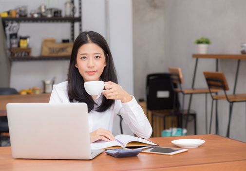 Beautiful asian young woman working online on laptop and drink coffee sitting at coffee shop, professional female freelancer using notebook computer with connect to internet for distance job.