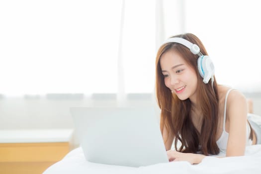 Beautiful asian young woman relax listening to music with headphone and laptop online internet on vacation in bedroom, cheerful of asia girl leisure, lifestyle concept.